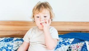 Interior portrait of a cute toddler boy biting nails